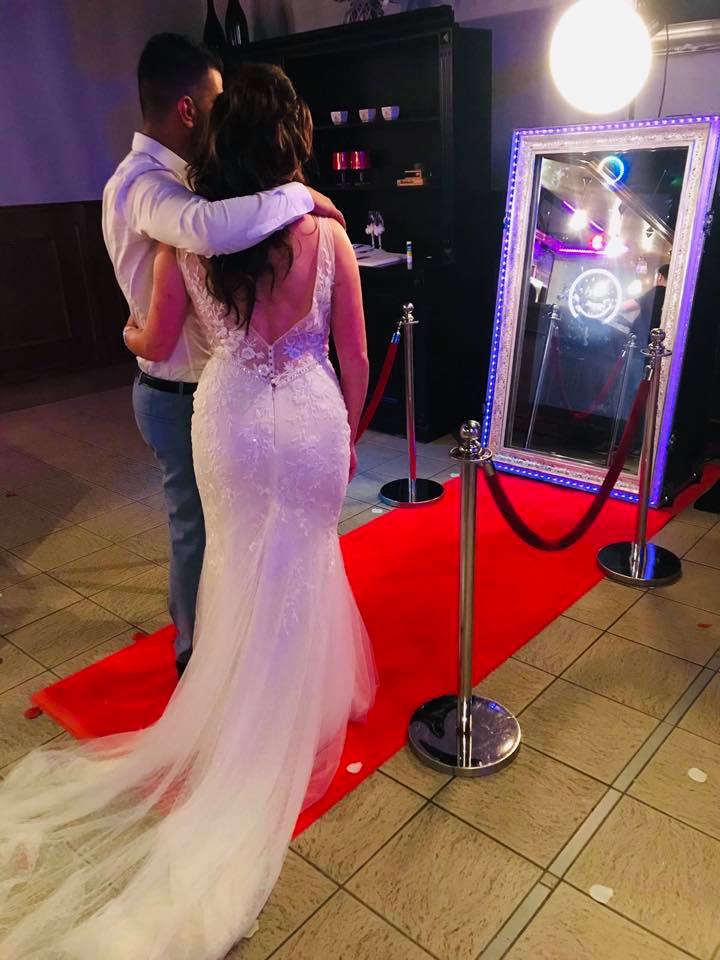 Detail van de Spiegel photobooth: hand raakt het verborgen touchscreen aan op het spiegeloppervlak met gouden ornament.