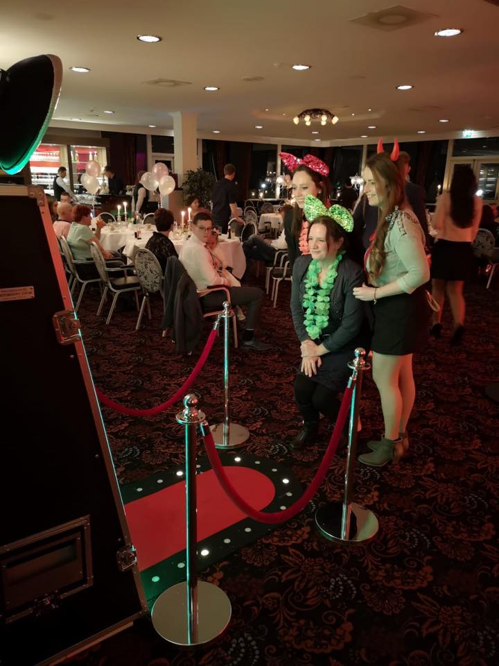 Vier gasten poseren vrolijk voor de grote Spiegel photobooth; de feestzaal op de achtergrond is zacht verlicht.